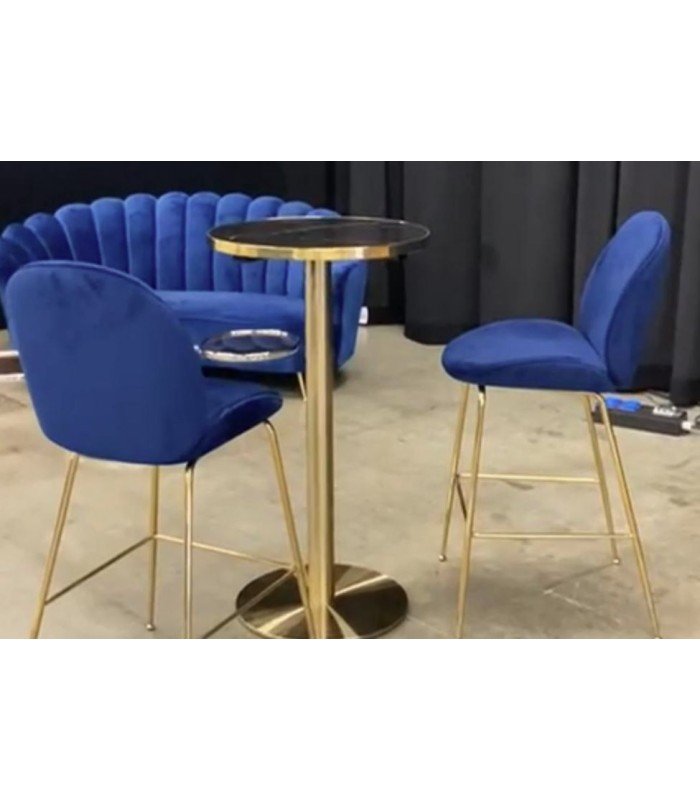 Deux chaises de bar bleu en velours avec pieds dorés autour d’une table haute, canapé assorti en arrière-plan