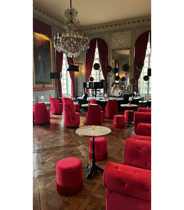 Castle salon furnished with red velvet barrel chairs, poufs and pedestal tables under a chandelier, 126 Events
