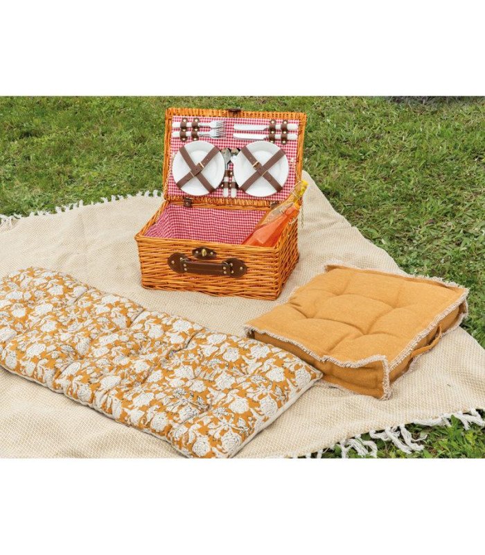 malle à pique-nique en osier vintage ouverte, posée sur une nappe dans un jardin, avec vaisselle apparente