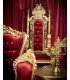 Gilded wooden throne and red velvet in front of a red curtain on a stage with matching armchair and coffee table