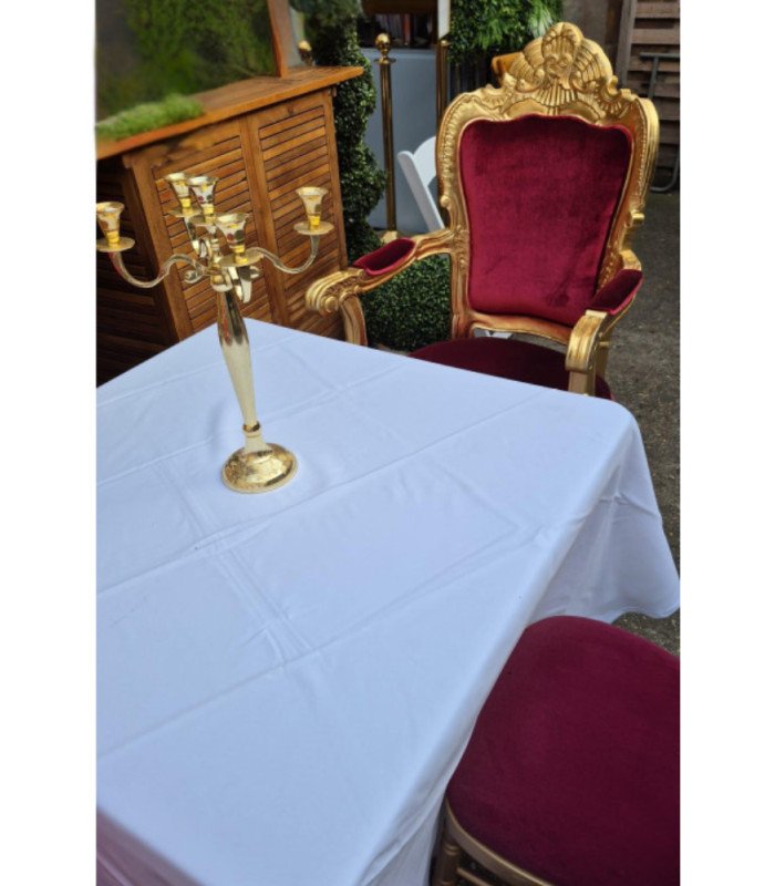 Golden and red baroque-style armchair arranged around a table covered with a tablecloth and a candlestick for a reception